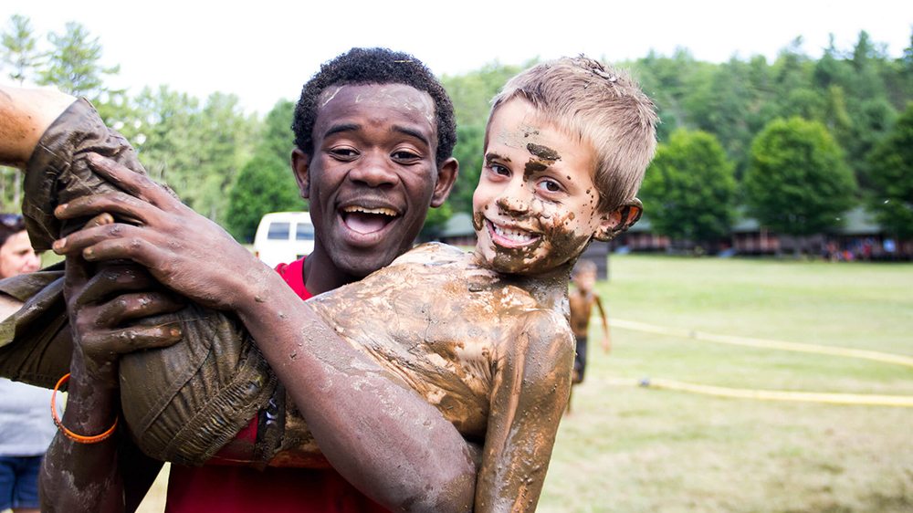 Man holding a kid in his arms after they were in the mud pit.