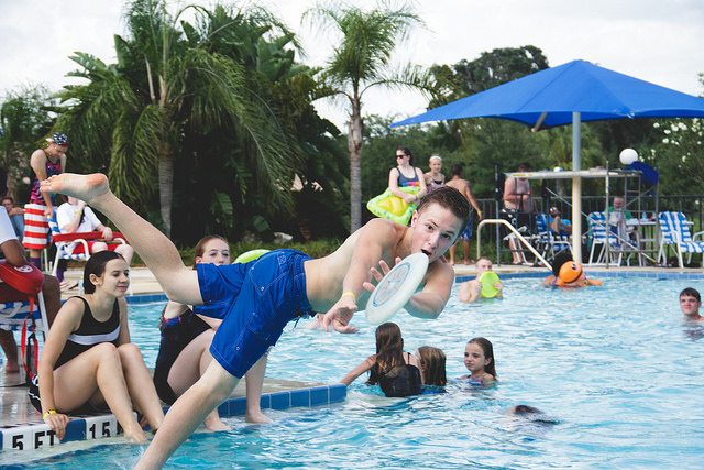 kid catching a Frisbee while jumping into a pool.