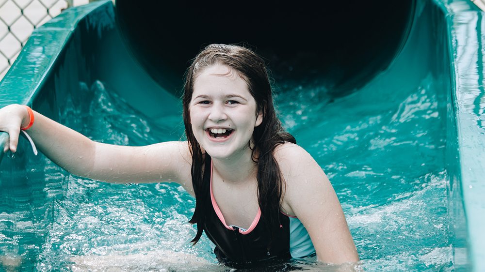 Girl getting out of the bottom of a water slide smiling.