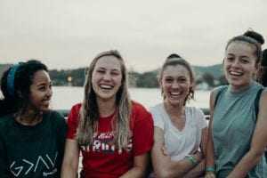Four girls smiling with a lake in the background.